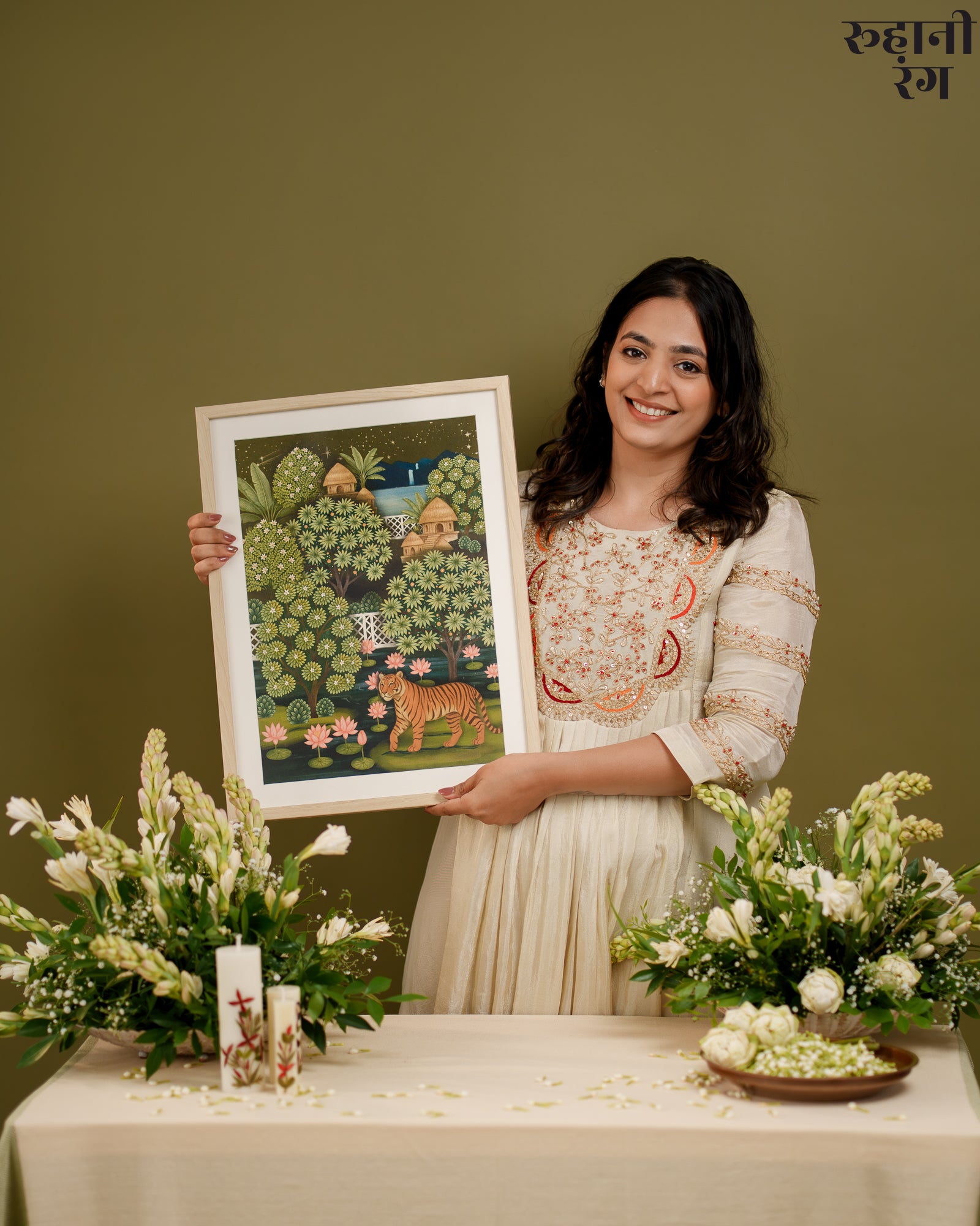 Woman holding a framed artwork with a green background, surrounded by flowers and decor.