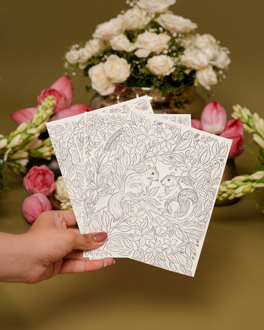 Hand holding two white cards with black patterns in front of floral arrangements on a brown background