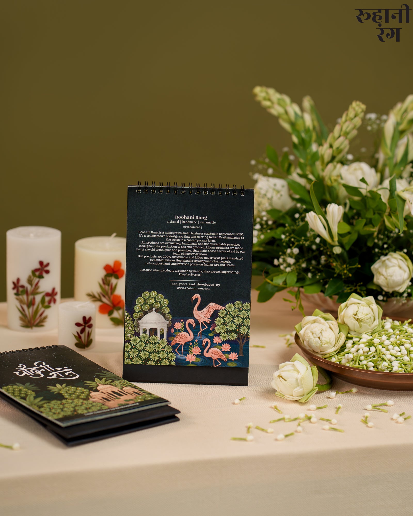 Decorative calendar with floral and flamingo design on a table with candles and flowers.
