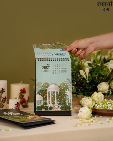 Hand holding a calendar with garden design on a table with flowers and candles.