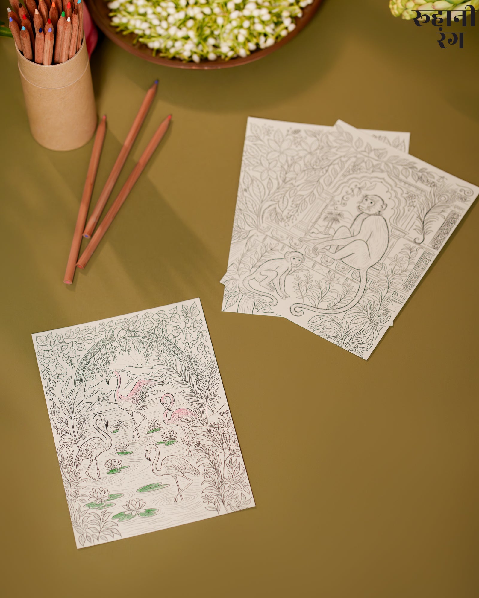 Two coloring sheets with animal designs on a brown surface, accompanied by colored pencils.