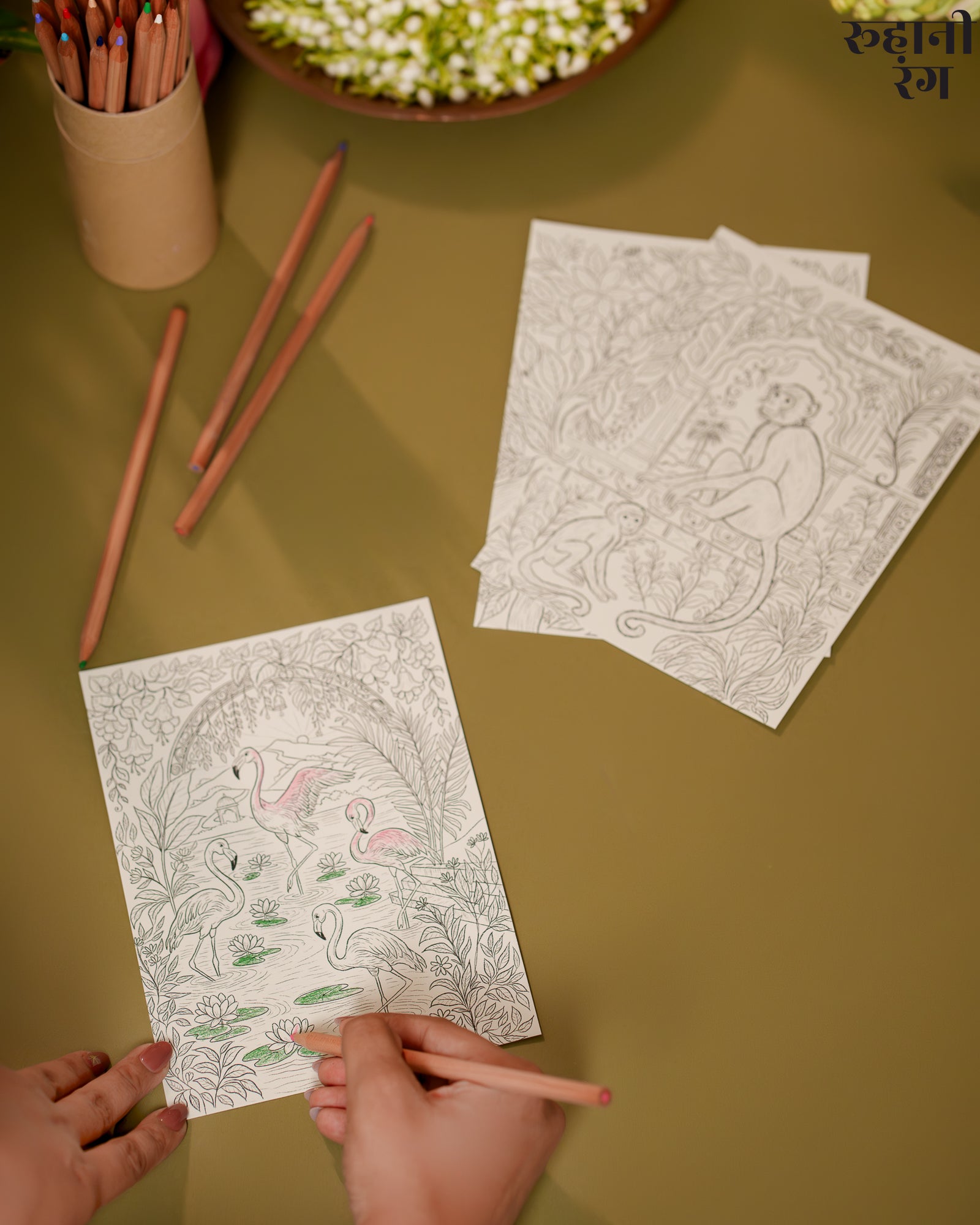 Coloring book pages with illustrations on a brown surface with pencils and flowers.